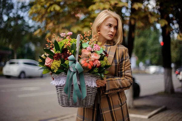 Słodkie blondynka kobieta trzyma wiklinowy koszyk z różne kwiaty i wygląda na stronie — Zdjęcie stockowe