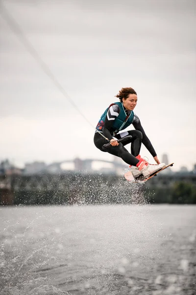 Femme en combinaison tenant la corde et sautant professionnellement par-dessus l'eau sur wakeboard — Photo