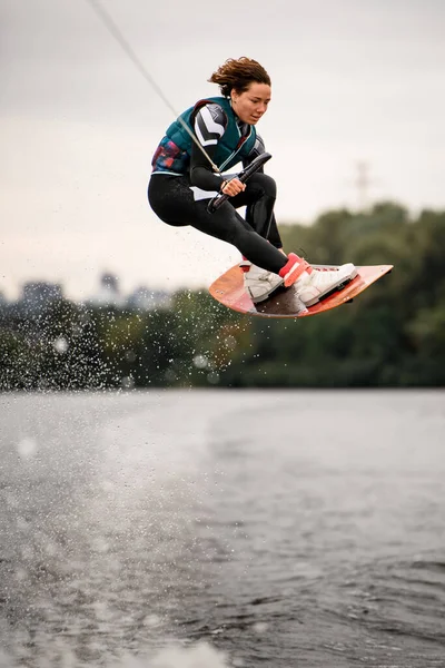 Femme en combinaison tenant la corde et sautant magistralement par-dessus l'eau sur wakeboard — Photo