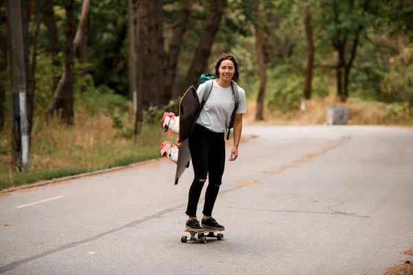 Vrolijk vrouw in wit t-shirt paardrijden skateboard met wakeboard in haar hand. — Stockfoto