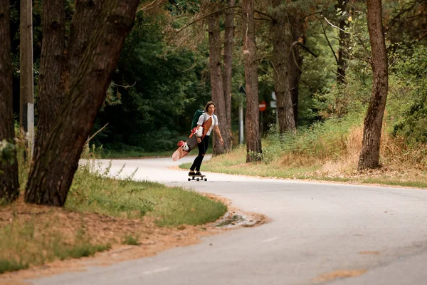 Vista da estrada ao longo da qual a jovem cavalga no skate com wakeboard em sua mão — Fotografia de Stock