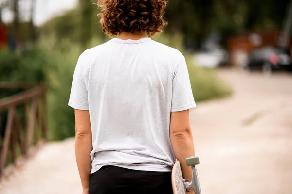 Achteraanzicht van mooie jonge vrouw in wit t-shirt met skateboard — Stockfoto