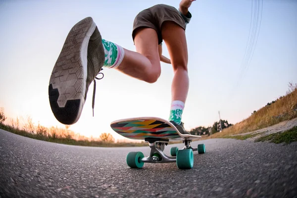 Visão de baixo ângulo da menina que está montando no skate no asfalto. — Fotografia de Stock