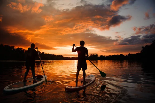 Back view of man and woman on sup boards floating on river — Stock Photo, Image