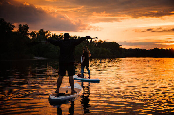 man and woman float along the river standing on sup boards with oars