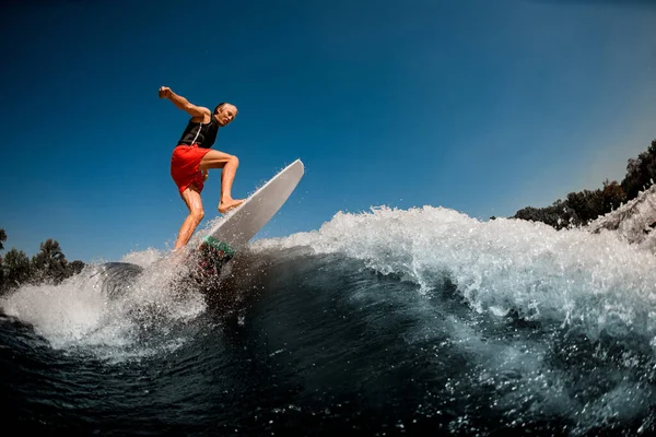 Energetischer athletischer Mann balanciert aktiv auf Wakeboard im Surfstil auf plätschernder Welle. — Stockfoto