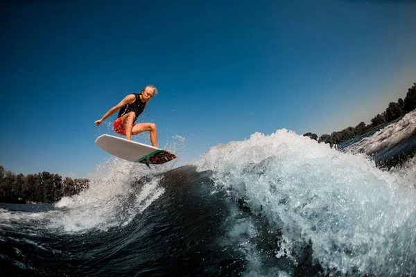 Hombre rebota en wakeboard estilo surf sobre salpicar ola contra el cielo azul —  Fotos de Stock