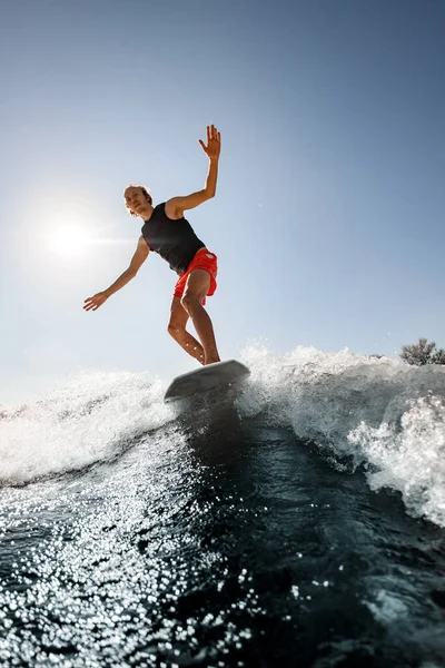 Homem bonito desce a onda no wakeboard estilo surf no dia ensolarado — Fotografia de Stock