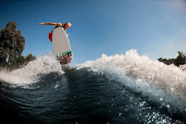 Энергичный человек прыгает высоко на волне на вейкборде в стиле серфинга — стоковое фото