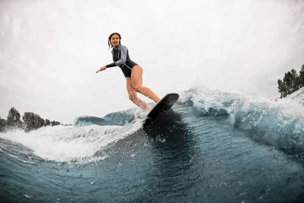 Frau im schwarzen Neoprenanzug steht auf Surfbrett und reitet auf Welle — Stockfoto