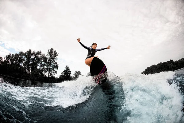 Mujer activa en traje de neopreno negro cabalga sobre tabla de surf en ola —  Fotos de Stock