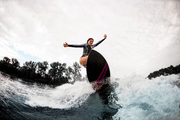 Жіночий шок-серфер в чорному гідрокостюмі їде на дошці для серфінгу на хвилі — стокове фото