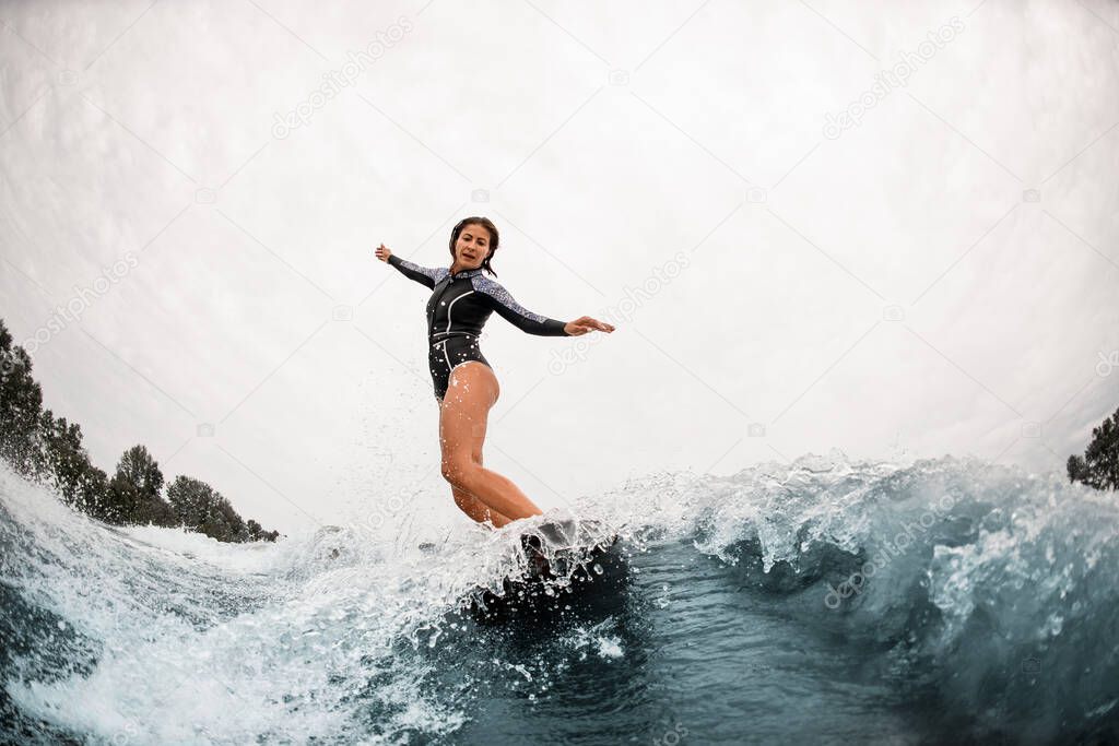 active woman in black wetsuit balancing on a surfboard on a wave