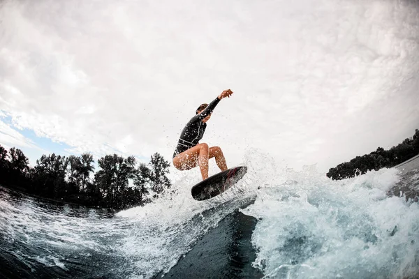 アクティブスポーツ女性で黒ウェットスーツ効果的にジャンプオンサーフボード上の波 — ストック写真