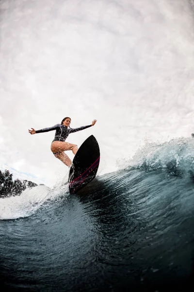 アクティブ女性で黒ウェットスーツ専門的に乗る上のサーフボード上の波 — ストック写真