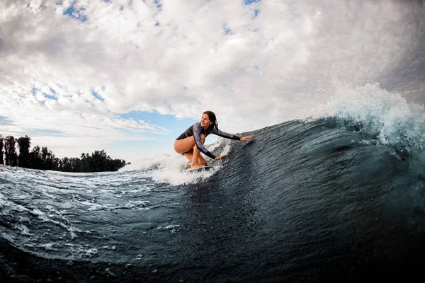 Вид на жінку, яка їде на хвилі, сидячи на дошці для серфінгу і торкаючись води рукою . — стокове фото