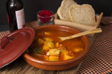Rioja tarzında patates tabağının sunumu. Geleneksel İspanyol yemekleri kil bir tencerede sunuluyor ve ekmek ve çiçeğin yanında tahta bir kaşık.