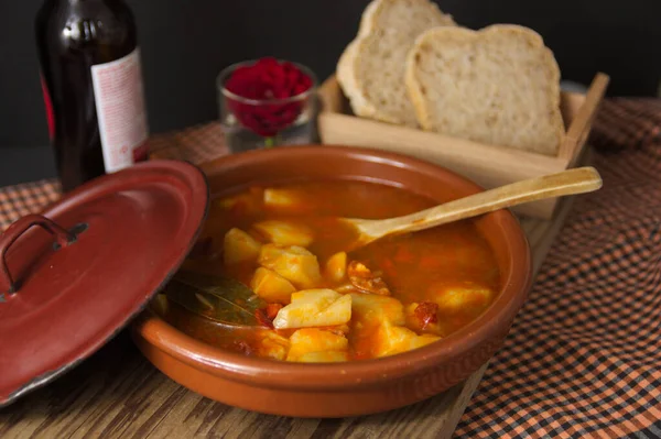 Rioja tarzında patates tabağının sunumu. Geleneksel İspanyol yemekleri kil bir tencerede sunuluyor ve ekmek ve çiçeğin yanında tahta bir kaşık.