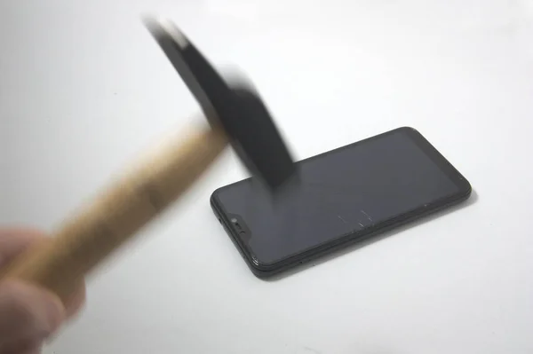 一个移动的铁锤的特写 它打破了一个被隔离在白色桌子上的手机的屏幕 — 图库照片
