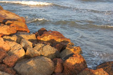 Bir hendeğin kayaları, gün batımında aydınlanan denizin dalgalarını durdurmak için.