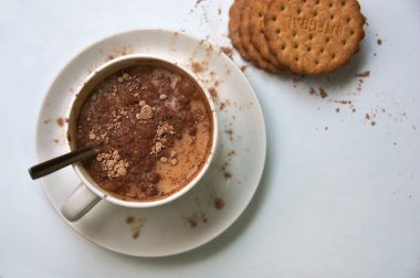 Bir kase sütlü, çözünür kakaolu ve tam tahıllı kurabiyelerin yanında bir masa manzarası.