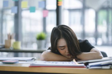 Ofisinde işyerinde uyuyan yorgun ve bitkin genç iş kadını