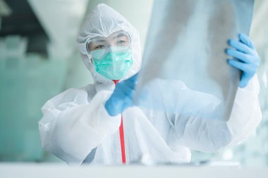 Koruyucu kıyafetli bir doktor, koğuş hastanesindeki hastanın göğüs röntgenini kontrol ediyor. Corona virüsü Covid-19 Kavramı.
