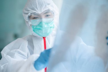 Koruyucu kıyafetli bir doktor, koğuş hastanesindeki hastanın göğüs röntgenini kontrol ediyor. Corona virüsü Covid-19 Kavramı.