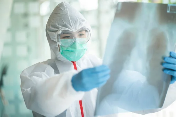 Medical Doctor with protective suit checking examining chest x-ray film of patient at ward hospital. Corona virus Covid-19 Concept.