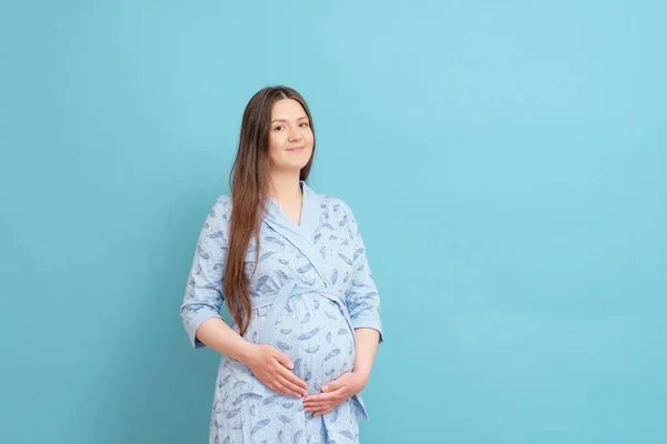 young happy pregnant woman on blue background in blue home bathrobe