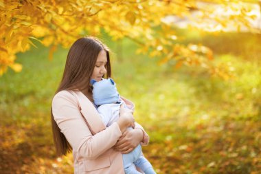 Anne ve bebeğin sonbahar parkındaki portreleri, anne bebeğe sarılıyor.