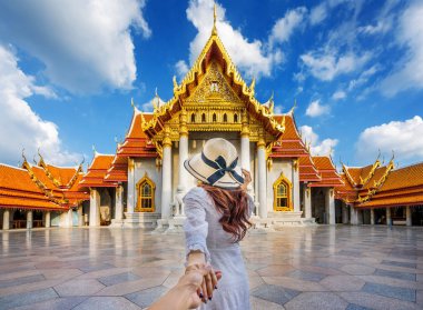 Women tourists holding man's hand and leading him to Wat Benchamabophit or the Marble Temple in Bangkok, Thailand. clipart
