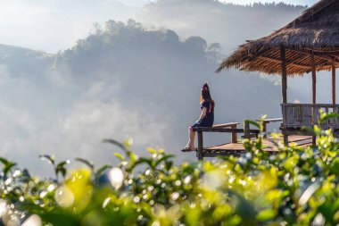 Tepe kabilesi kıyafeti giymiş bir kadın yeşil çay tarlasında kulübede oturuyor..