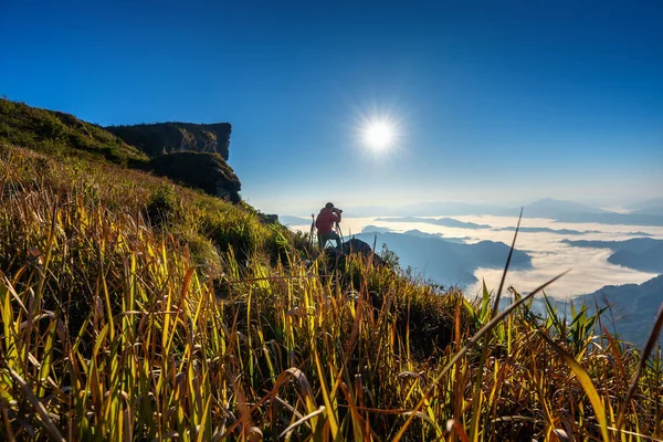 カメラマン手でカメラを握り、自然の中で岩の上に立つ。チェンライのプーチファ山脈, タイ — ストック写真