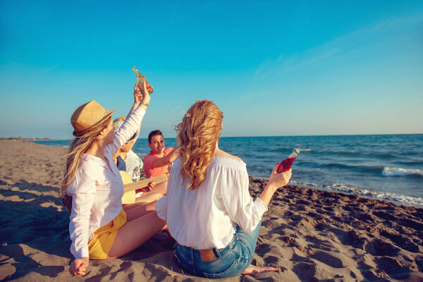 group of happy young people dancing at the beach on beautiful summer sunset