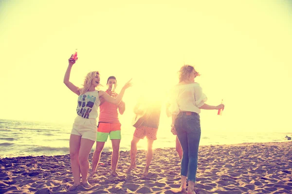 group of happy young people dancing at the beach on beautiful summer sunset