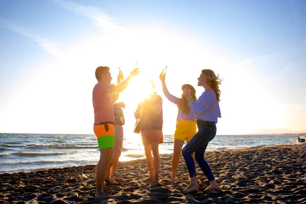 group of happy young people dancing at the beach on beautiful summer sunset