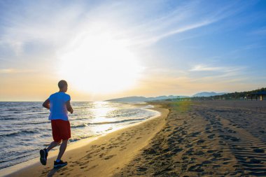 Tam uzunlukta dikiz kumsalda gün batımında koşan adam