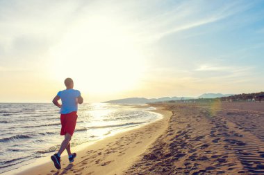 Tam uzunlukta dikiz kumsalda gün batımında koşan adam