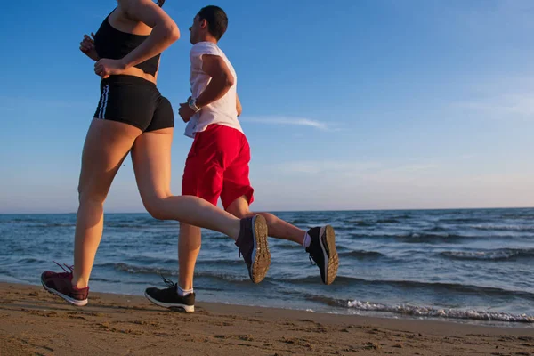 Low section view of young couple jogging on tropical beach at sunset