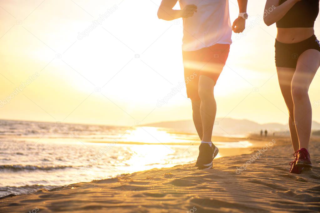 Low section view of young couple jogging on tropical beach at sunset