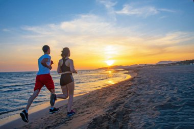Günbatımında tropik plajda koşan erkek ve kadınlar