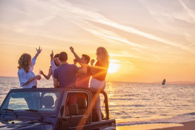 Bir grup genç insan batımında sahilde arabada eğleniyor