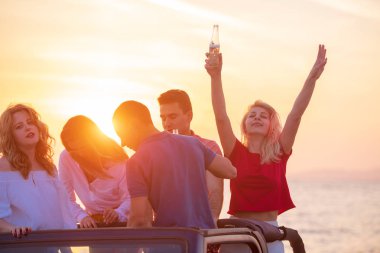 Bir grup genç insan batımında sahilde arabada eğleniyor