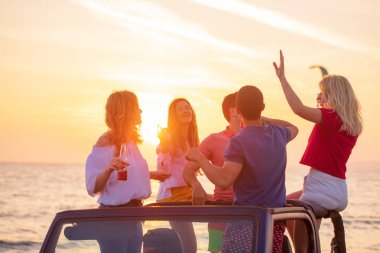 Bir grup genç insan batımında sahilde arabada eğleniyor