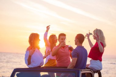 Bir grup genç insan batımında sahilde arabada eğleniyor