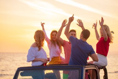 Bir grup genç insan batımında sahilde arabada eğleniyor
