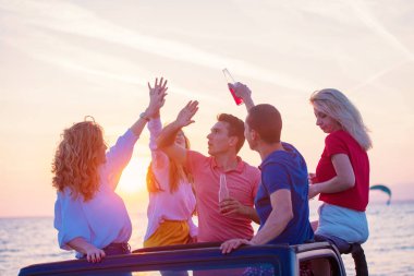 Grup günbatımı sırasında sahilde Cabrio araba içinde eğleniyor içecekler genç insan