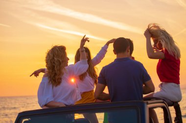 Grup günbatımı sırasında Plajı'nda Cabrio araba içinde eğleniyor içecekler genç insan