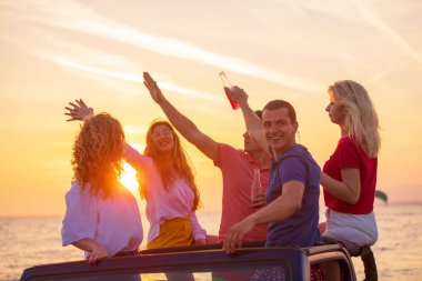 Grup günbatımı sırasında sahilde Cabrio araba içinde eğleniyor içecekler genç insan